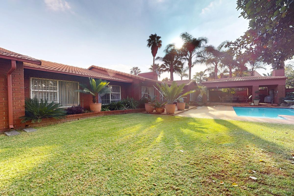 Rear view of the property featuring a well-maintained lawn, a swimming pool, and a covered patio area attached to the brick house.