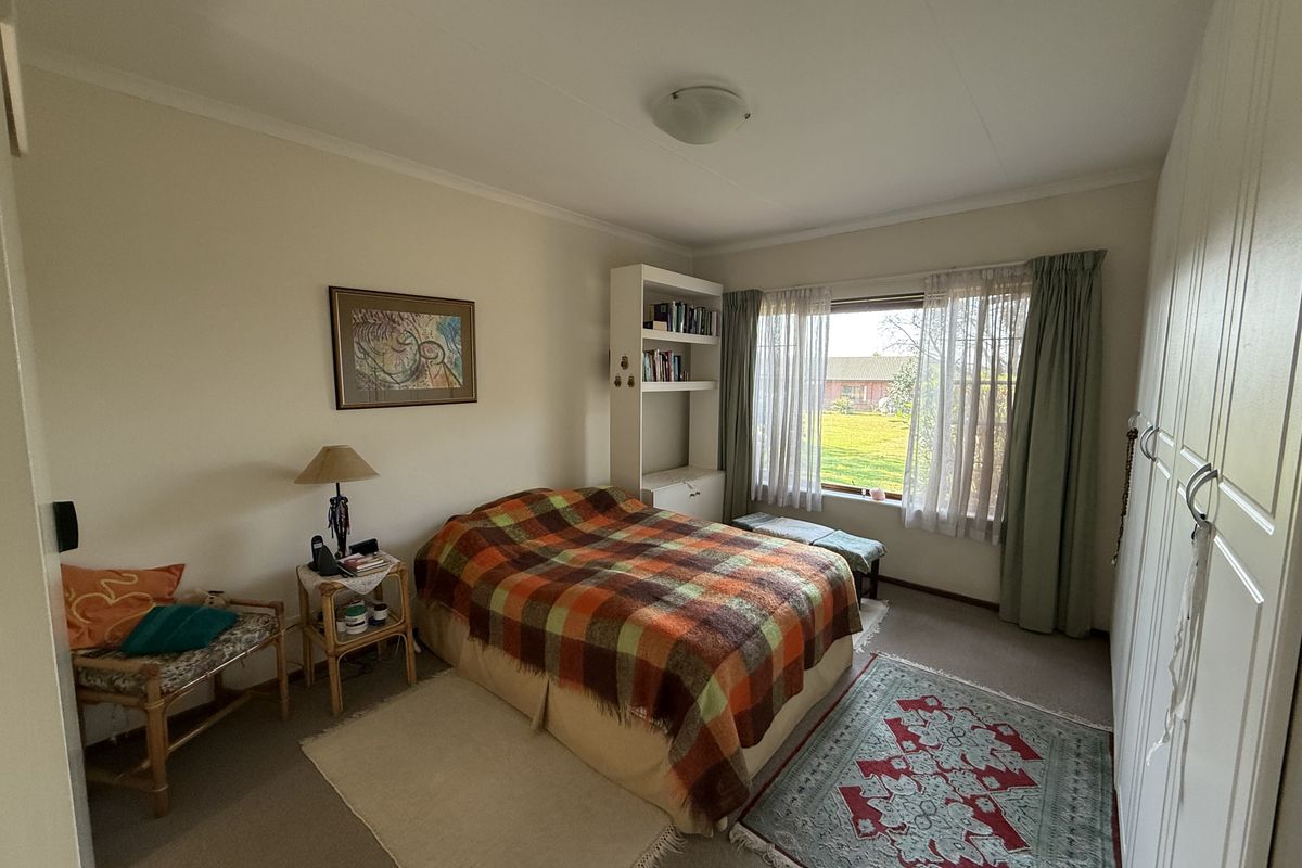 A functional bedroom featuring built-in wardrobes, carpeted flooring, and a large window providing natural light and garden views.