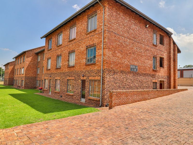 Exterior view of a multi-story face brick apartment building featuring a paved driveway and well-maintained lawn area.