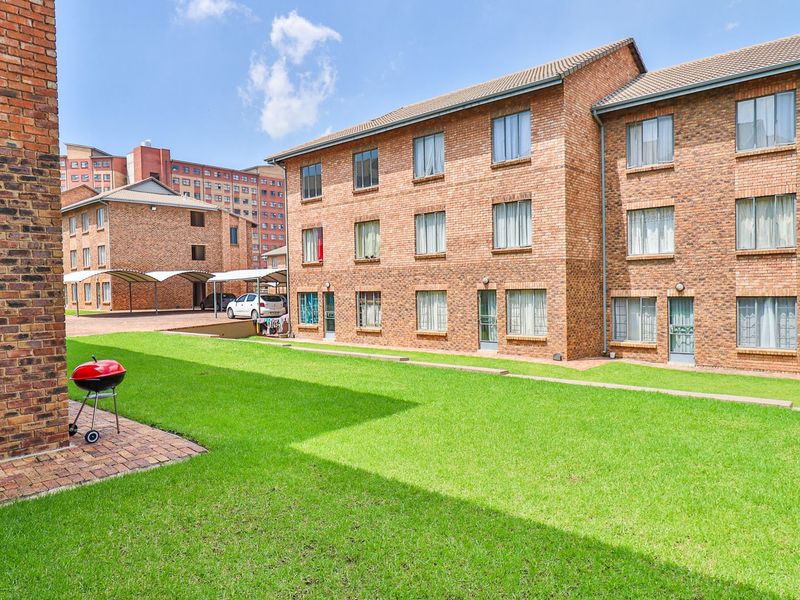 A view of the rear exterior of a multi-story face brick apartment complex featuring a well-maintained lawn and paved walkways.