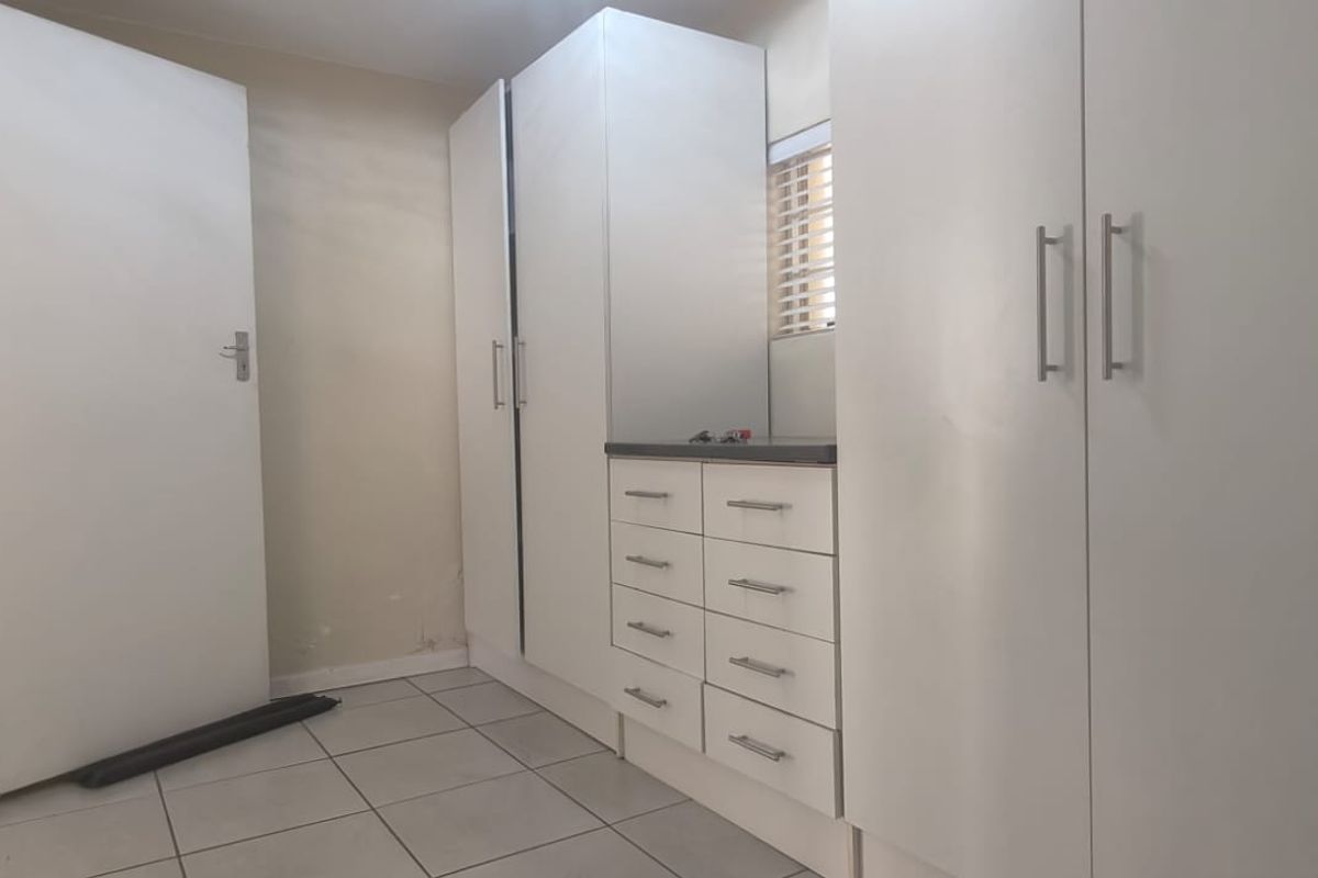 A functional bedroom featuring built-in white cabinetry with integrated drawers and tiled flooring, offering a clean and neutral space ready for personalization.