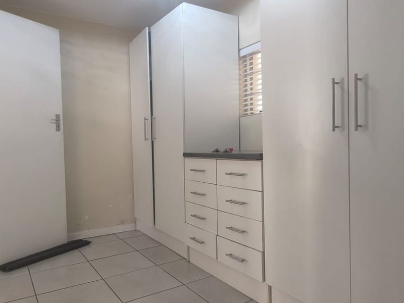 A functional bedroom featuring built-in white cabinetry with integrated drawers and tiled flooring, offering a clean and neutral space ready for personalization.