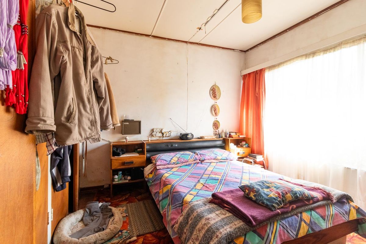 A bedroom featuring dated finishes, including worn flooring and ceiling panels, with natural light from a large window.