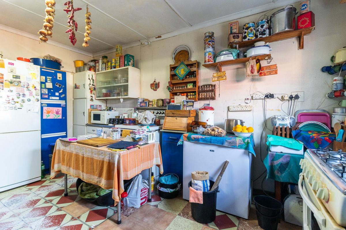 A dated kitchen featuring original cabinetry, tiled flooring, and a functional layout with built-in stove and storage shelving.