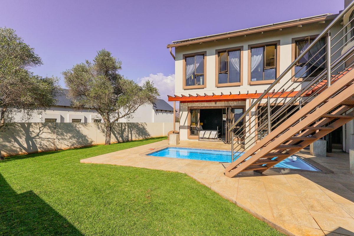 Rear view of the property featuring a swimming pool, stone paved patio, timber pergola, and an external staircase leading to the upper level.
