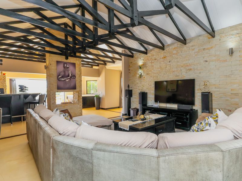 Spacious open-plan living area featuring a striking stone wall, exposed timber roof trusses, and a seamless flow into the adjacent kitchen.