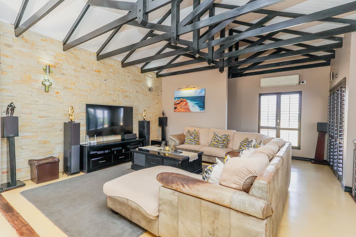 Spacious living room featuring a striking stone feature wall, high vaulted ceilings with exposed timber trusses, and direct access to outdoor areas via french doors.