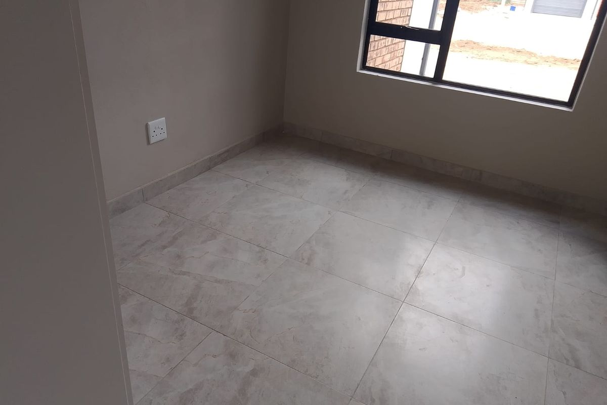 A clean, empty bedroom featuring neutral tiled flooring and a modern aluminium window frame, providing a blank canvas for interior design.