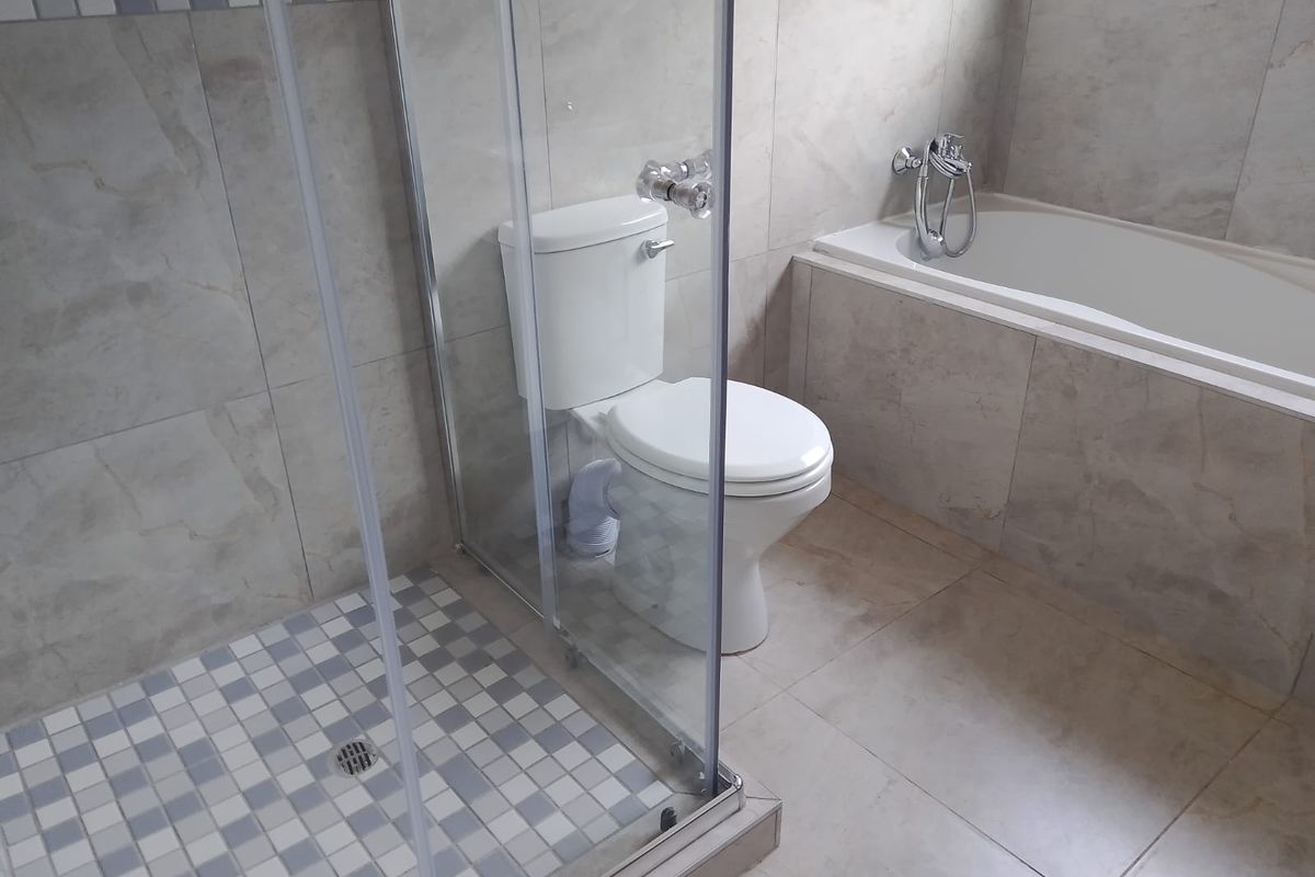 A clean, modern bathroom featuring a glass-enclosed shower, a built-in bathtub, and neutral wall tiling.