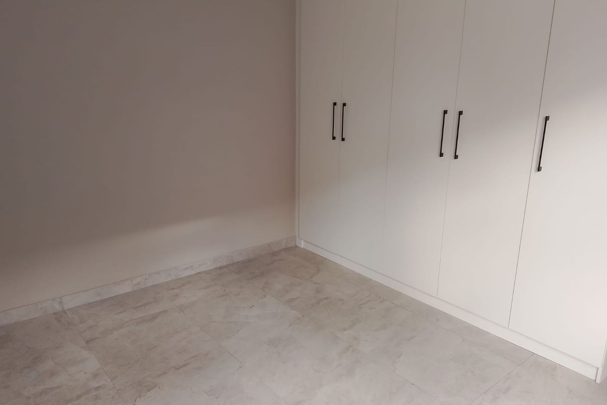 A clean, empty bedroom featuring modern built-in cupboards and neutral tiled flooring, offering a blank canvas for personalization.