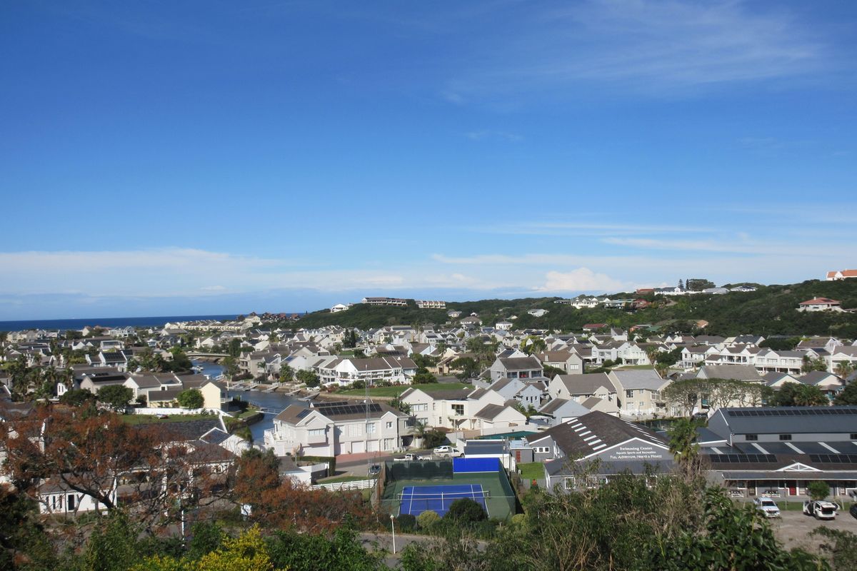 An elevated aerial view overlooking a residential estate, featuring a tennis court, community facilities, and surrounding coastal landscape.