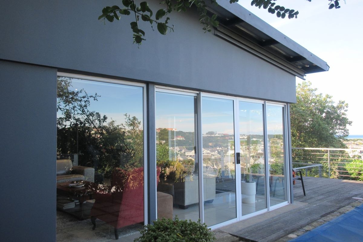 Exterior view of the rear facade featuring large sliding glass doors, a wooden deck, and a view of the surrounding neighborhood.