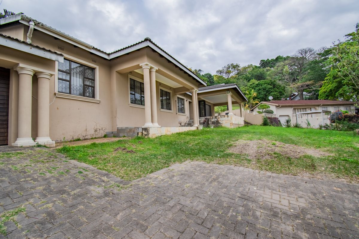 Rear view of the house featuring a paved driveway, covered patio area with columns, and established garden space.