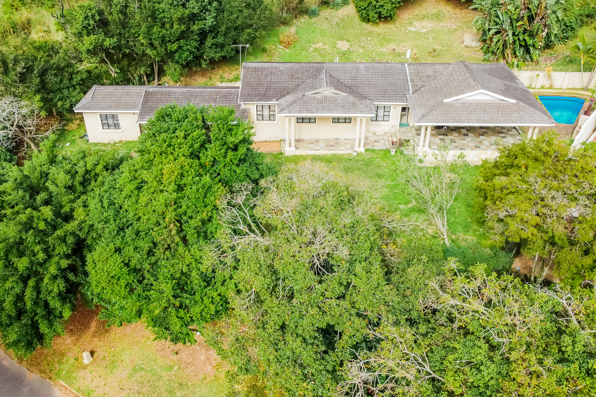 Aerial view of a residential property featuring a tiled roof, covered patio, and a swimming pool set within a lush, tree-filled garden.