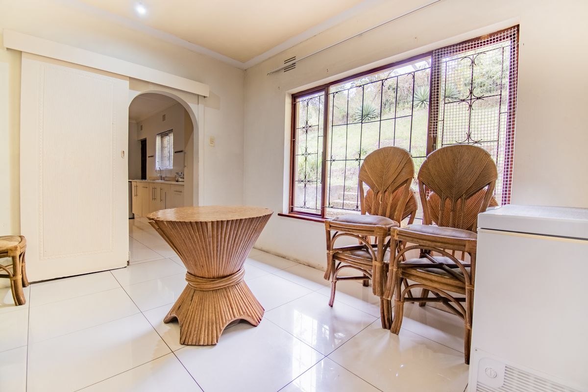 A bright living area featuring tiled flooring, an arched doorway leading to the kitchen, and large windows fitted with security bars.