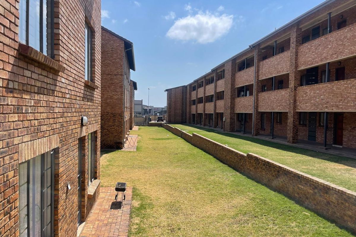 Exterior view of a multi-story apartment complex featuring face brick facades, communal lawn areas, and paved patio spaces.