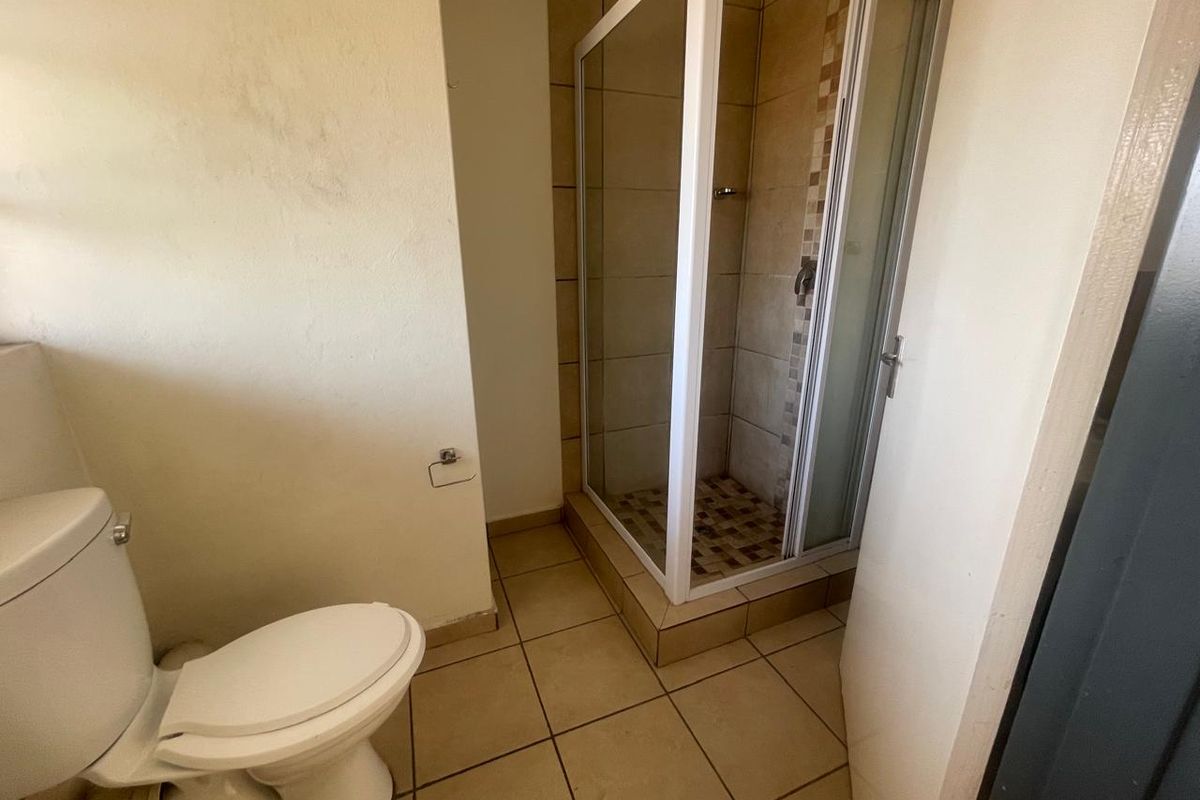 A functional bathroom featuring a tiled shower enclosure and standard toilet, with neutral floor tiling and painted walls.