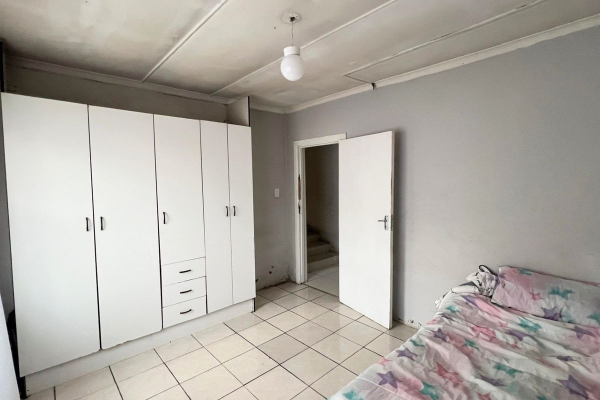 A bedroom featuring tiled flooring and a built-in wardrobe, requiring some cosmetic attention to the ceiling and wall finishes.