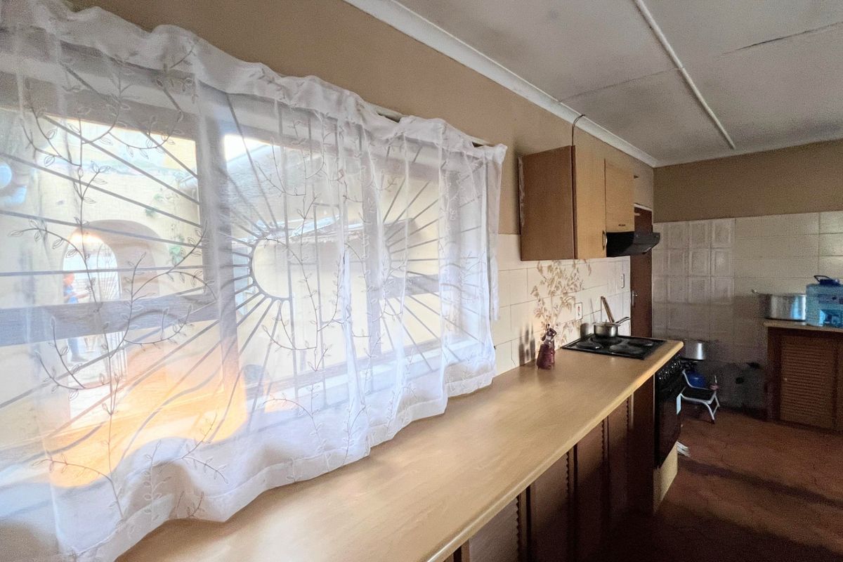 A functional kitchen featuring built-in cabinetry, laminate countertops, a hob with extractor fan, and tiled splashbacks, offering potential for modernization.