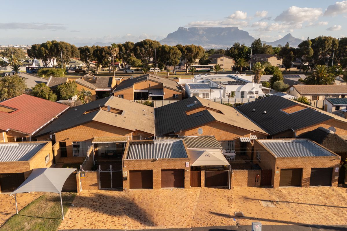 Aerial view of a residential complex featuring brick facades, tiled roofs, and paved driveways with Table Mountain visible in the background.
