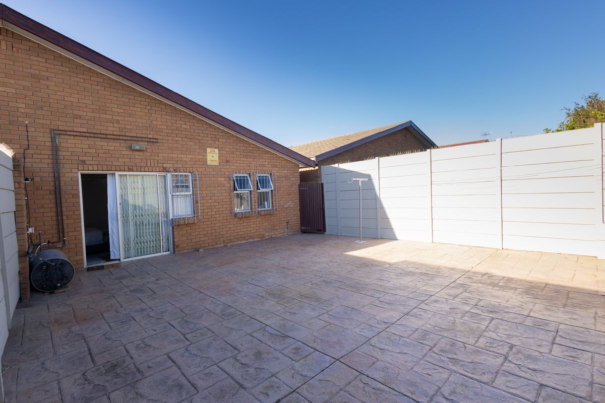 A paved rear courtyard area featuring face-brick exterior walls, sliding door access, and secure precast concrete perimeter walling.