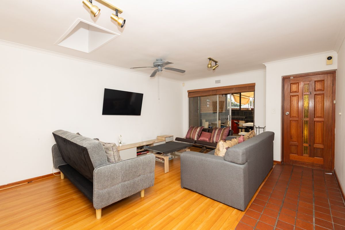 A living room featuring laminate wood flooring, a ceiling fan, and a wooden entrance door, with direct access to an outdoor patio area.