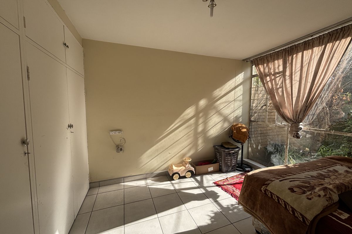A bedroom featuring tiled flooring, built-in cupboards, and a large window with security bars, offering natural light and potential for modernization.