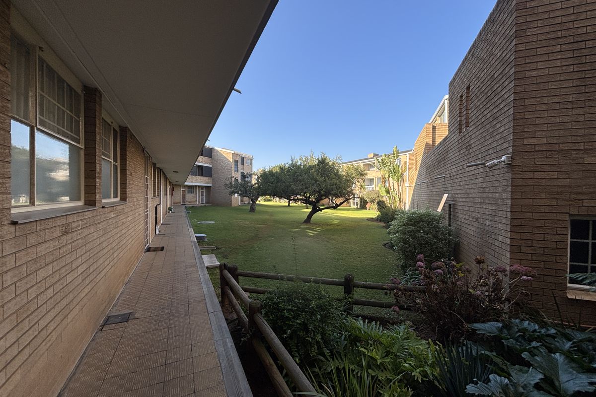 A view of the communal garden area and paved walkway between townhouse blocks, featuring established trees and brick exterior walls.