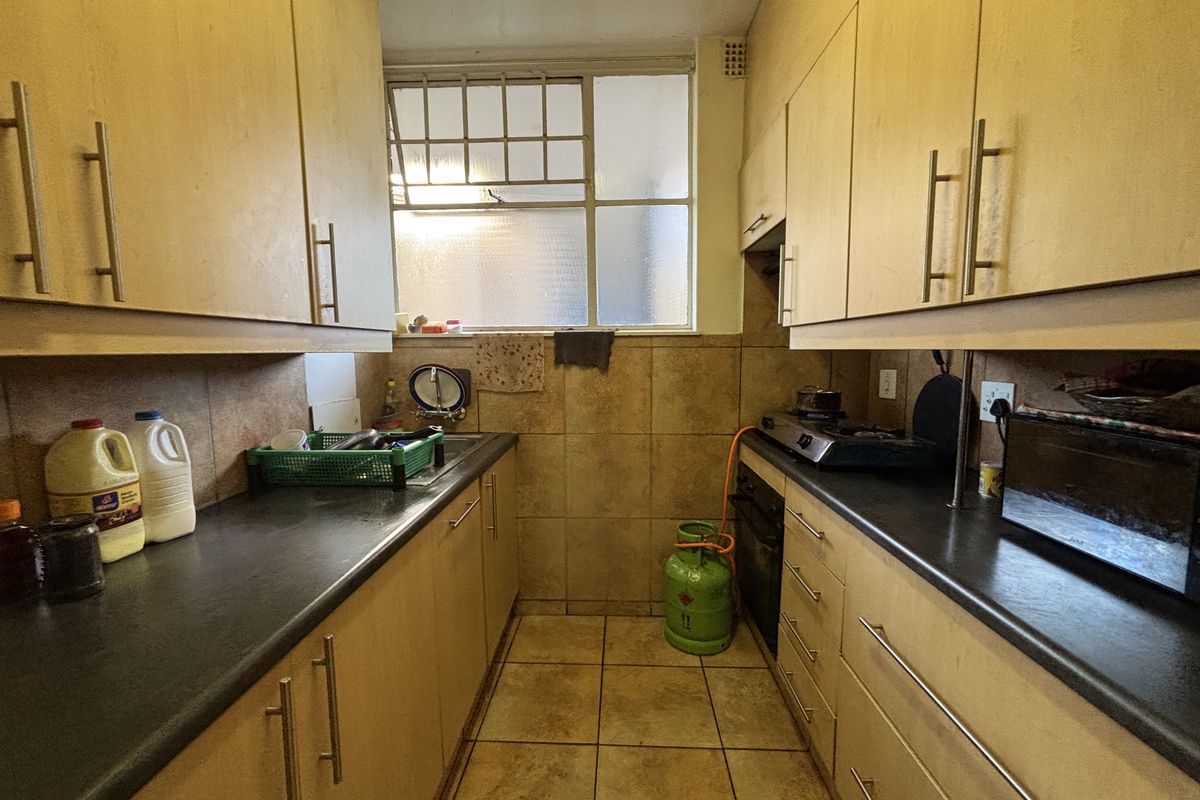 A compact galley-style kitchen featuring laminate cabinetry, tiled surfaces, and built-in cooking appliances, offering a functional layout with potential for modern updates.