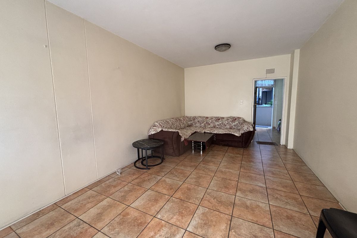 A living room featuring ceramic floor tiles and neutral wall finishes, providing a functional space with direct access to an adjoining area.