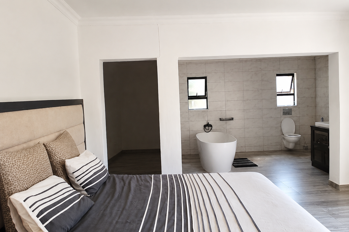 Spacious bedroom featuring an open-plan en-suite bathroom with a modern freestanding bathtub, wall-mounted toilet, and vanity unit.
