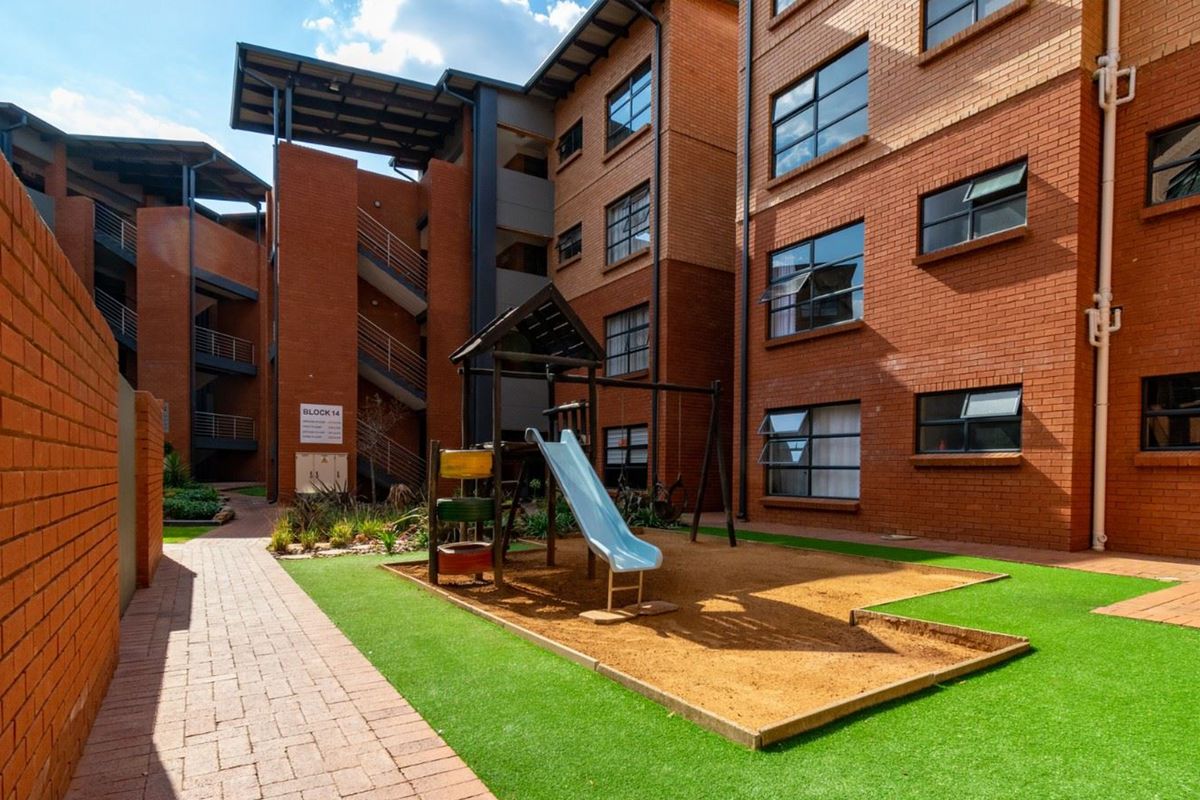 A well-maintained apartment complex courtyard featuring brick facades, paved walkways, artificial grass, and a communal children's play area.