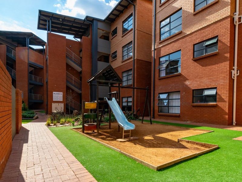 A well-maintained apartment complex courtyard featuring brick facades, paved walkways, artificial grass, and a communal children's play area.