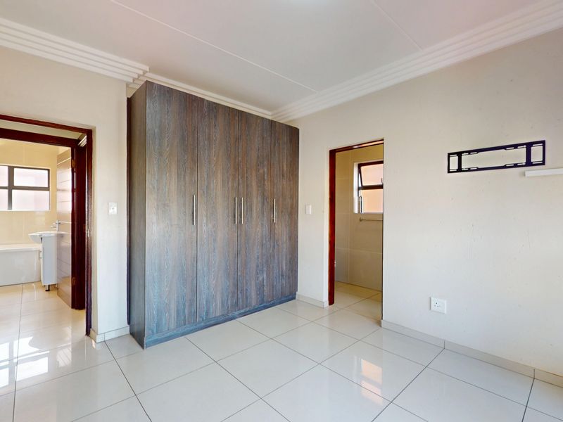 A bright, empty bedroom featuring neutral tiled flooring, built-in wooden cupboards, and direct access to an en-suite bathroom.