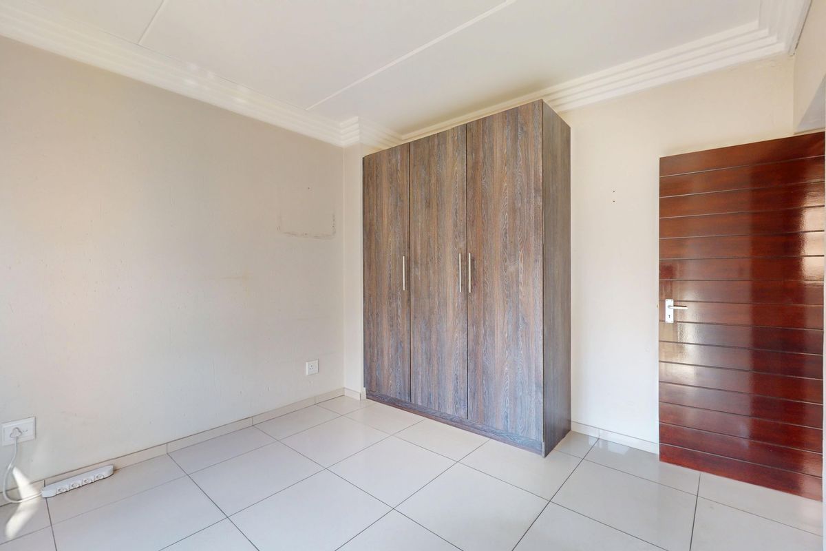 A clean, empty bedroom featuring neutral tiled flooring, a built-in wooden wardrobe, and a solid timber door.