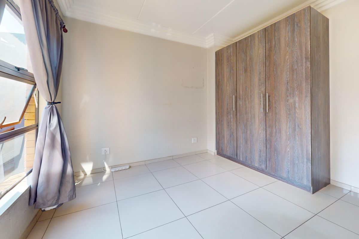 A bright, empty bedroom featuring neutral tiled flooring, a large built-in wooden wardrobe, and decorative ceiling cornicing.