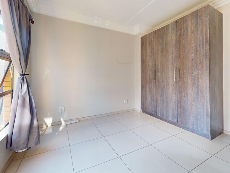A bright, empty bedroom featuring neutral tiled flooring, a large built-in wooden wardrobe, and decorative ceiling cornicing.