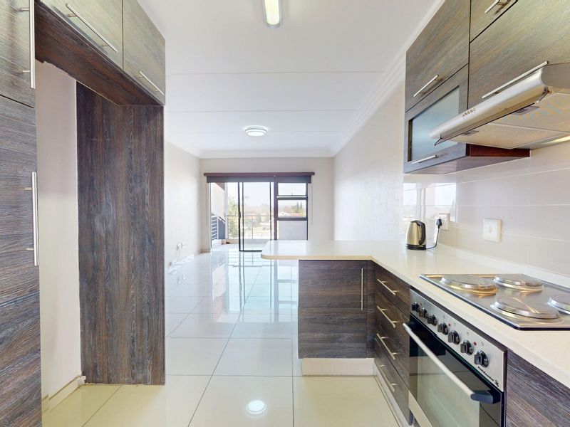 Modern open-plan kitchen and living area featuring dark wood-grain cabinetry, stone countertops, integrated appliances, and sleek tiled flooring leading to a balcony.
