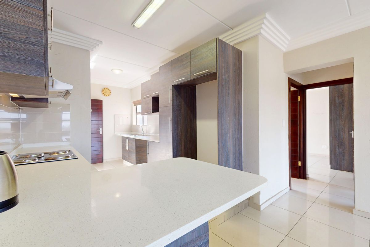 Modern kitchen featuring sleek dark wood cabinetry, light quartz countertops, an integrated electric hob, and clean tiled flooring in an open-plan layout.