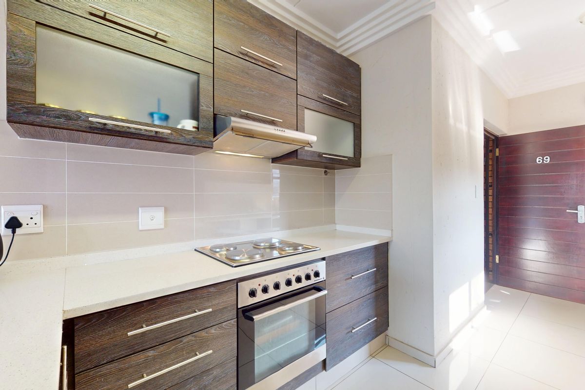 Modern kitchen featuring dark wood-grain cabinetry, stone countertops, integrated electric hob, oven, and extractor fan with neutral tiled backsplash and flooring.