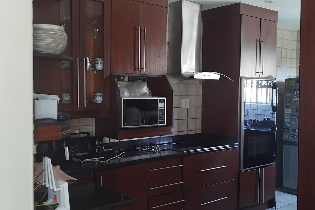 A functional kitchen featuring dark wood cabinetry, granite countertops, a stainless steel extractor fan, and a built-in oven with a tiled backsplash.