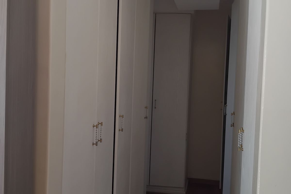 A bedroom interior featuring floor-to-ceiling built-in cupboards with light wood-grain finish and decorative handles.