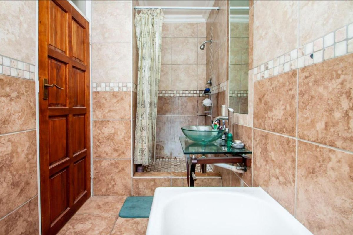 A compact bathroom featuring a glass vessel sink, a shower with a curtain, and floor-to-ceiling tiled walls.