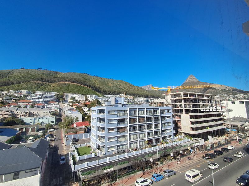Elevated urban view overlooking a residential apartment complex, surrounding neighborhood, and mountain landscape under a clear blue sky.