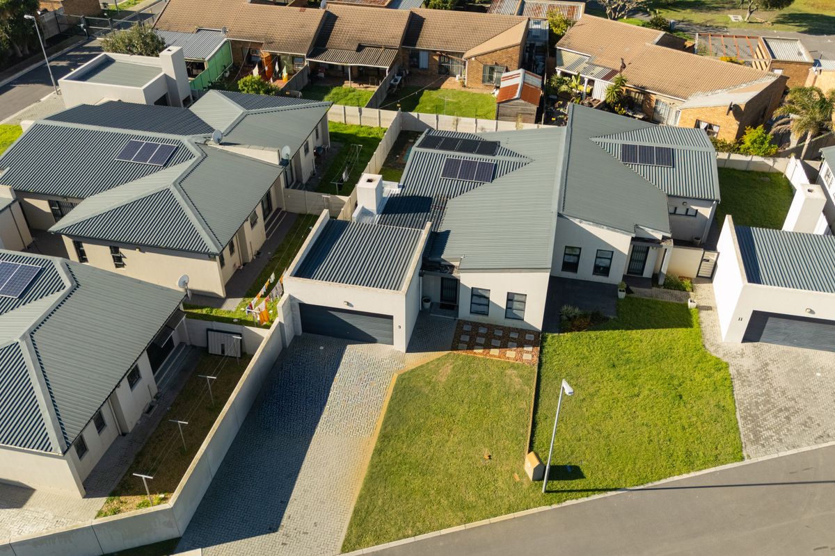 Aerial view of a modern townhouse complex featuring corrugated metal roofs, integrated solar panels, paved driveways, and private garden spaces.