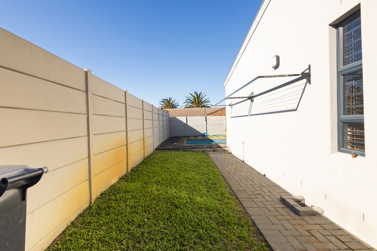 Rear exterior view of the townhouse featuring a paved walkway, a small lawn area, a wall-mounted clothesline, and a swimming pool in the background.