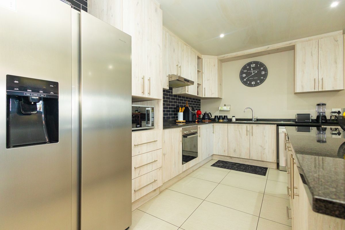 Modern kitchen featuring light wood-grain cabinetry, dark granite countertops, a subway tile backsplash, and integrated stainless steel appliances.