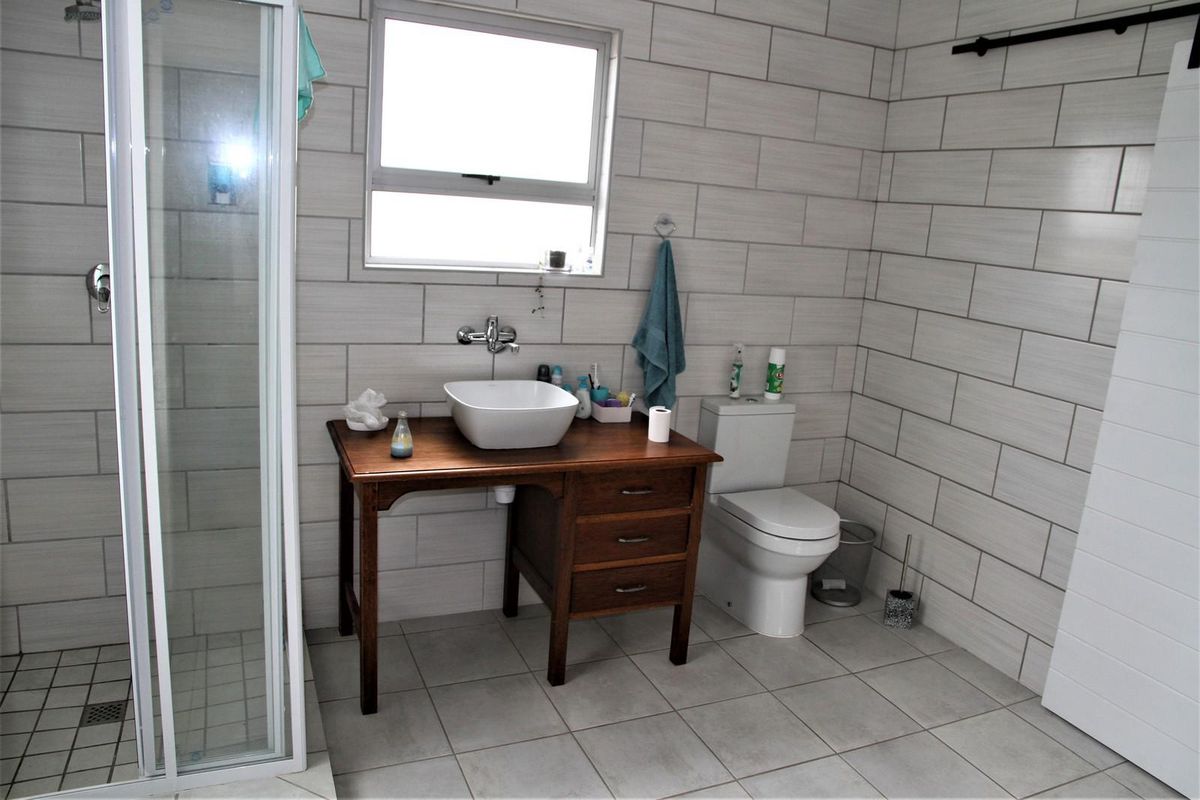 A modern bathroom featuring floor-to-ceiling wall tiles, a glass-enclosed shower, a toilet, and a unique wooden vanity with a vessel sink.