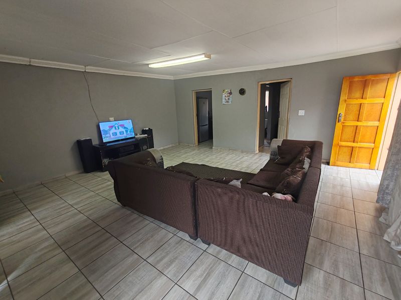 A spacious living room featuring tiled flooring, neutral wall finishes, and direct access to adjacent rooms through internal doorways.
