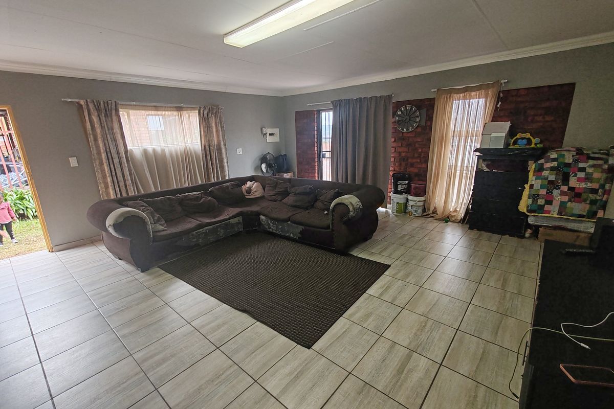 Spacious living room featuring neutral floor tiles, large windows for natural light, and a feature brick wall, offering a versatile layout for family living.